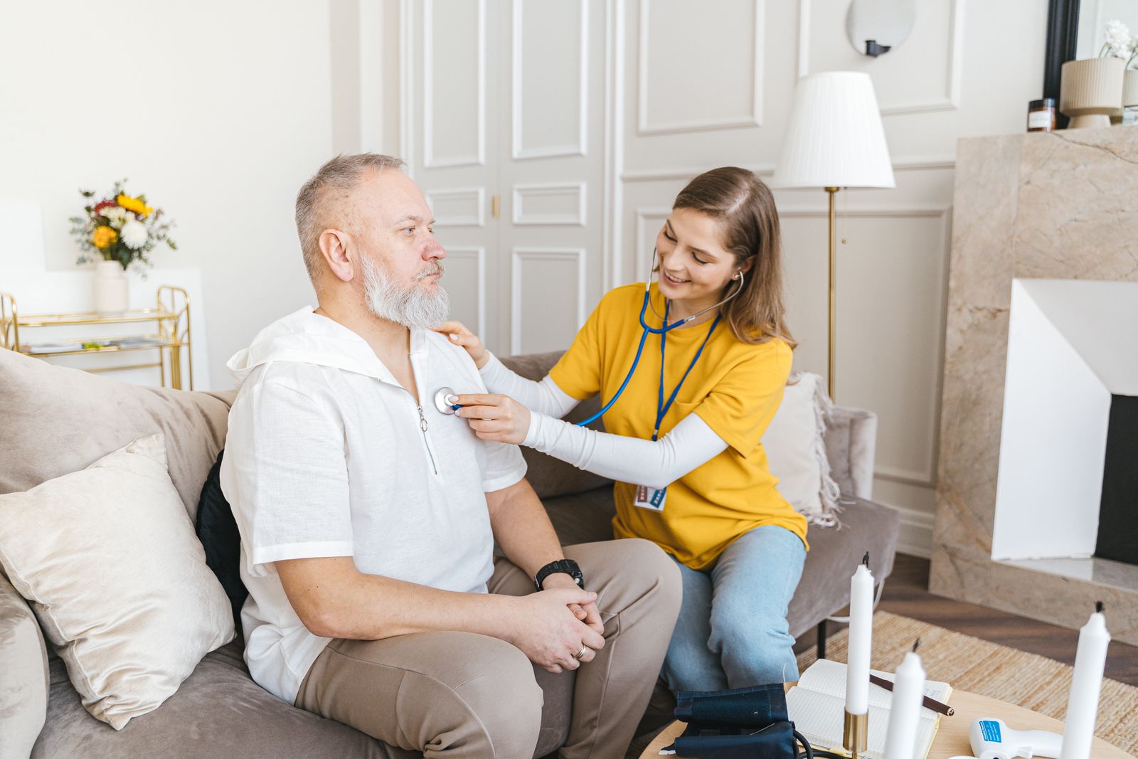 A visiting nurse checking an older man’s chest at home
