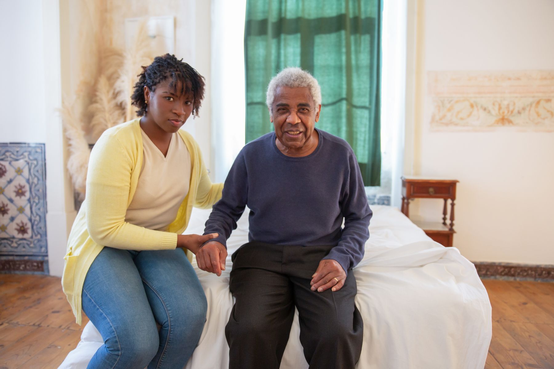 A PowerCare care worker sitting with an older man, holding his hand